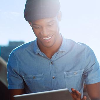 Man wearing a blue button up shirt and a flat cap smiling at a tablet